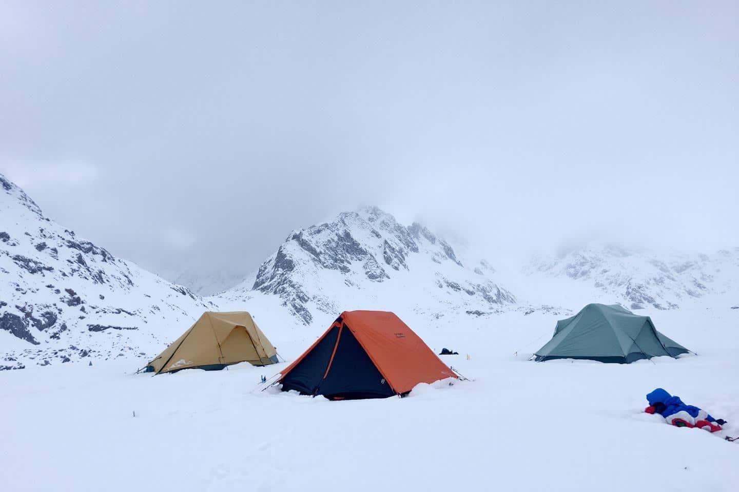 Trois tentes colorées dans un paysage montagneux enneigé